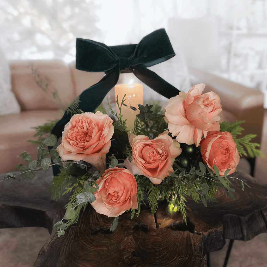 Christmas Centrepiece with peach garden roses and  green velvet ribbon wrapped around a glass candle holder and glass lights filled with moss twinkling